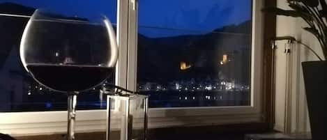 A glass of red wine on a table near a window with a view of a cityscape at night.