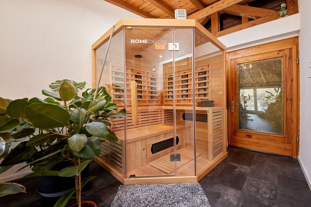 A corner room with a glass-enclosed sauna, wooden shelves, and a potted plant.