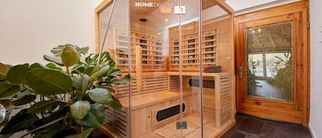 A corner room with a glass-enclosed sauna, wooden shelves, and a potted plant.