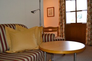 Ein Zimmer mit einem gestreiften Sofa, einem runden Holztisch, einer Stehlampe, einem gerahmten Bild an der Wand und einem Fenster mit Vorhängen.