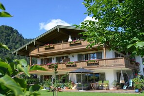 Un edificio de dos pisos con balcones, mesas al aire libre y un jardín.