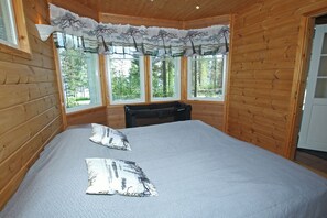 Ein Zimmer in einer Holzhütte mit einem Bett, zwei Kissen, einer Bank und großen Fenstern.