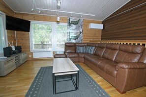 Ein gemütliches Wohnzimmer mit einem braunen Ledersofa, einem Holztisch und einem großen Fenster mit Blick auf Grünflächen.