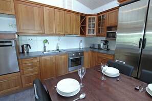 A modern kitchen with wooden cabinets, stainless steel appliances, and a dining table set for two. - Spacious Lakeside House at Koli – Sleeps 12 - Sauna - Skiing & Hiking (Koli)