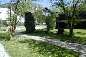 A pathway leading to a house with a white exterior, surrounded by greenery and a mountain in the background. - Holiday apartment with 1 bedroom (Walchensee)