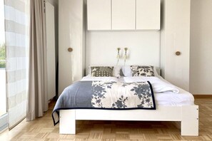 A bedroom with a bed, a window with curtains, a wall-mounted cabinet, and a bedside table. - Holiday apartment with 1 bedroom (Konstanz)