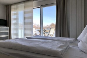 A hotel room with a bed, a television, and a view of the outdoors through large windows. - Holiday apartment with 1 bedroom (Konstanz)