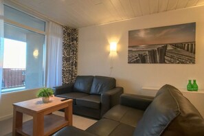 A living room with a sofa, a small table with a plant, a painting on the wall, and a window with curtains. - Apartment in Zoutelande with Wi-Fi (Zoutelande)