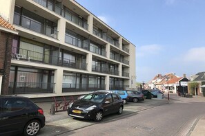 A multi-story residential building with balconies, parked cars, and a clear sky. - Apartment in Zoutelande with Wi-Fi (Zoutelande)