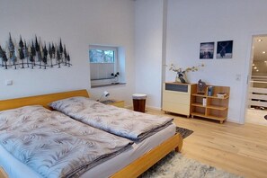 A bedroom with a large bed, a nightstand, a dresser, a window with blinds, a wall-mounted plant, and a shelf with decorative items. - EifeLeben Bad Münstereifel (Bad Münstereifel)