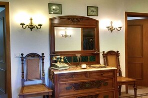 Een kamer met een houten dressoir, een stoel, een spiegel en wandlampen.