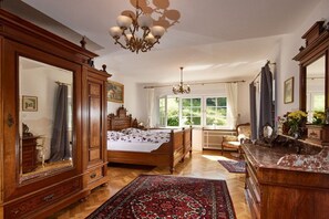 A bedroom with a large bed, wooden furniture, a chandelier, and a view of greenery outside. - Holiday apartment with 3 bedrooms (Nassau)