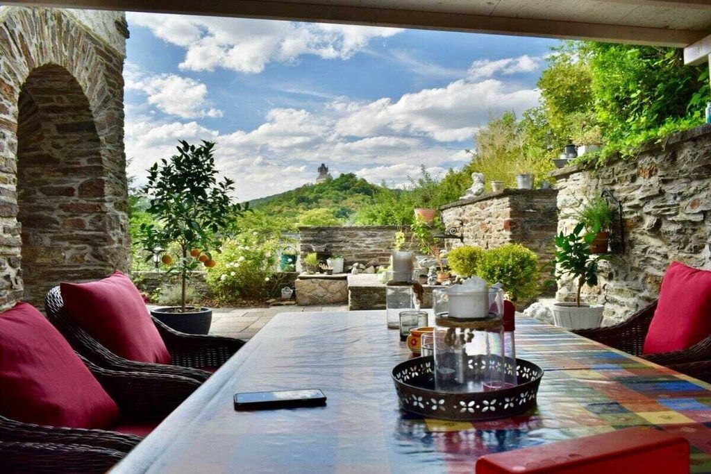 An outdoor seating area with wicker furniture, a table with a colorful tablecloth, and potted plants.