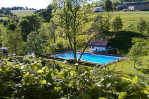 A swimming pool surrounded by lush greenery and houses in a rural setting. - Country House Jäger Holiday Apartment No. 2 (Todtnauberg)