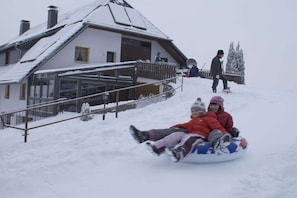 A snowy outdoor area with a building and a person walking in the background. - Holiday apartment with 2 bedrooms (St. Märgen)