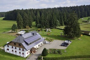 Un hotel con techo provisto de paneles solares, estacionamiento y un fondo de bosque.