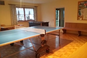A ping pong table in a room with a wooden floor, a window with curtains, and a bench. - Holiday apartment with 1 bedroom (Bad Hindelang)