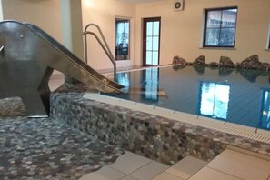 An indoor swimming pool with a stone border, a metal slide, and a view of the outside through a window. - Holiday apartment with 1 bedroom (Bad Hindelang)