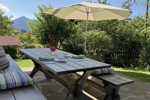 Un espace extérieur aménagé pour les repas, avec une table en bois, des bancs et un parasol.