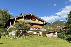 A multi-story wooden chalet with balconies, surrounded by lush greenery and mountains. - Holiday apartment with 1 bedroom (Fischbachau)