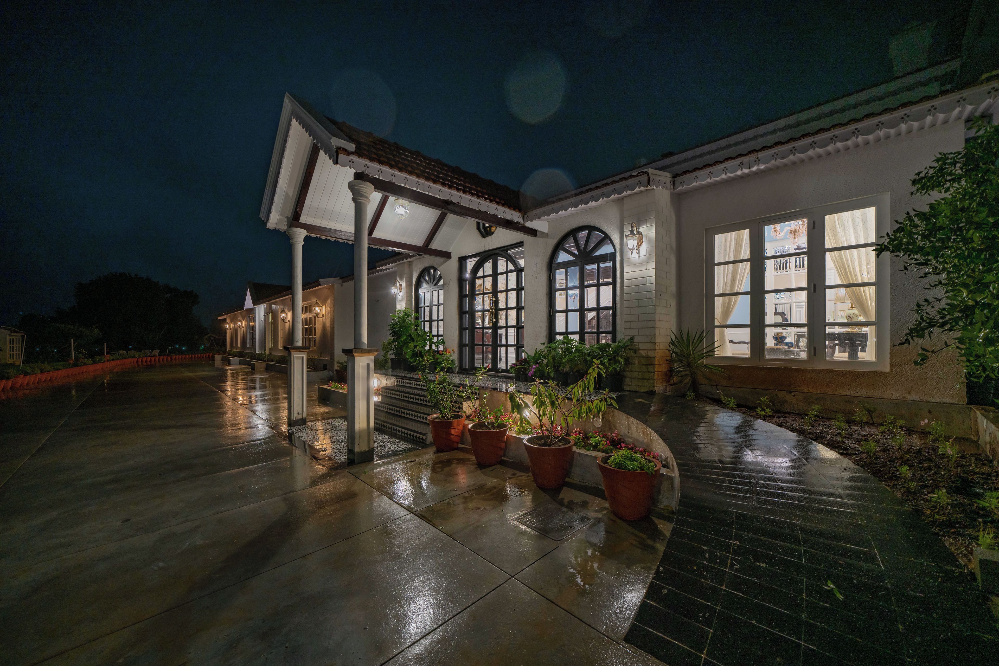 A building with a covered patio area, potted plants, and a wet floor indicating recent rain.