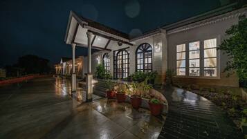 A building with a covered patio area, potted plants, and a wet floor indicating recent rain.