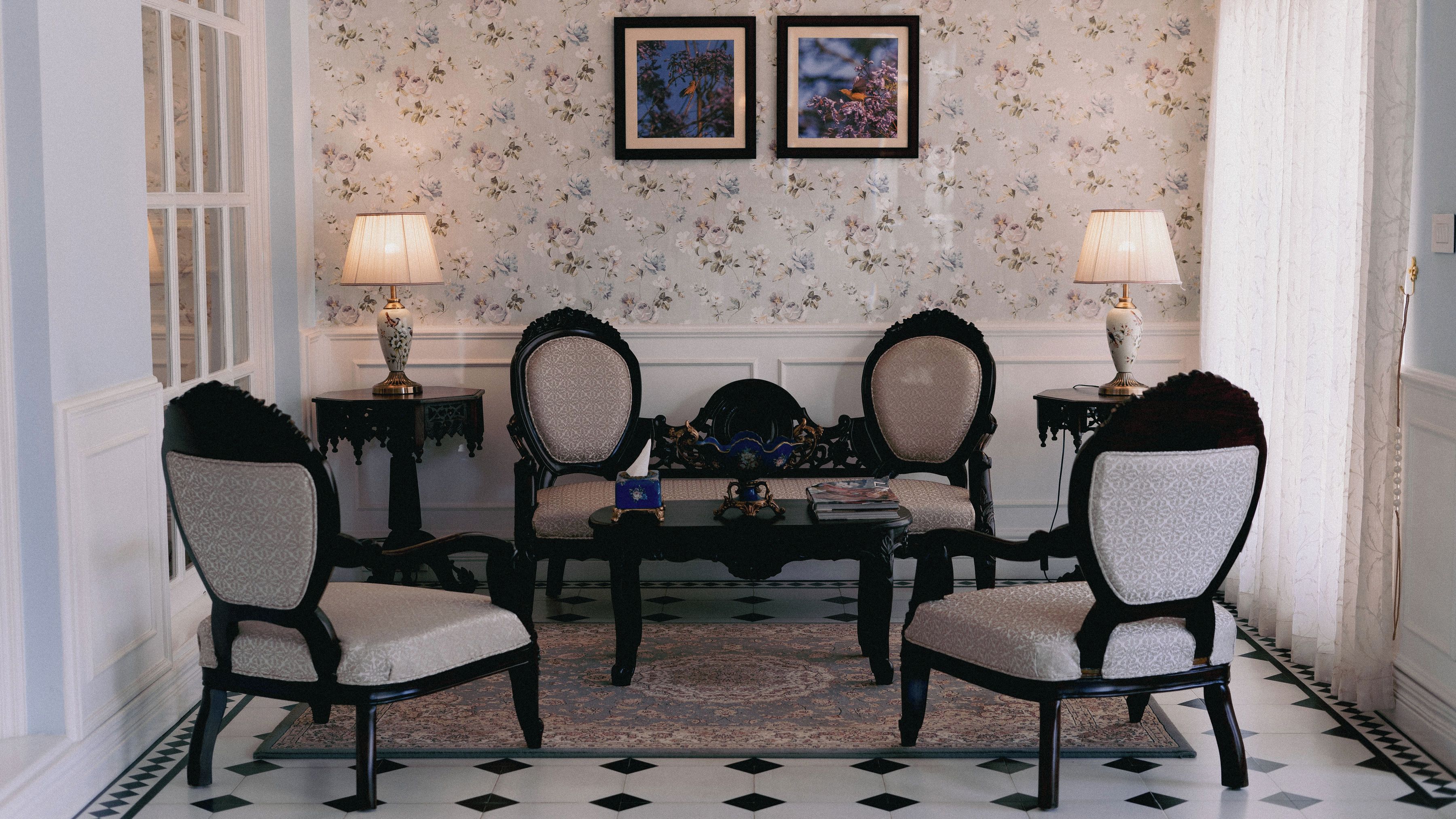 A formal sitting room with a round table, four chairs, two lamps, and two framed pictures on the wall.