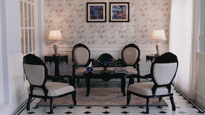 Un salón formal con una mesa redonda, cuatro sillas, dos lámparas y dos cuadros en la pared.