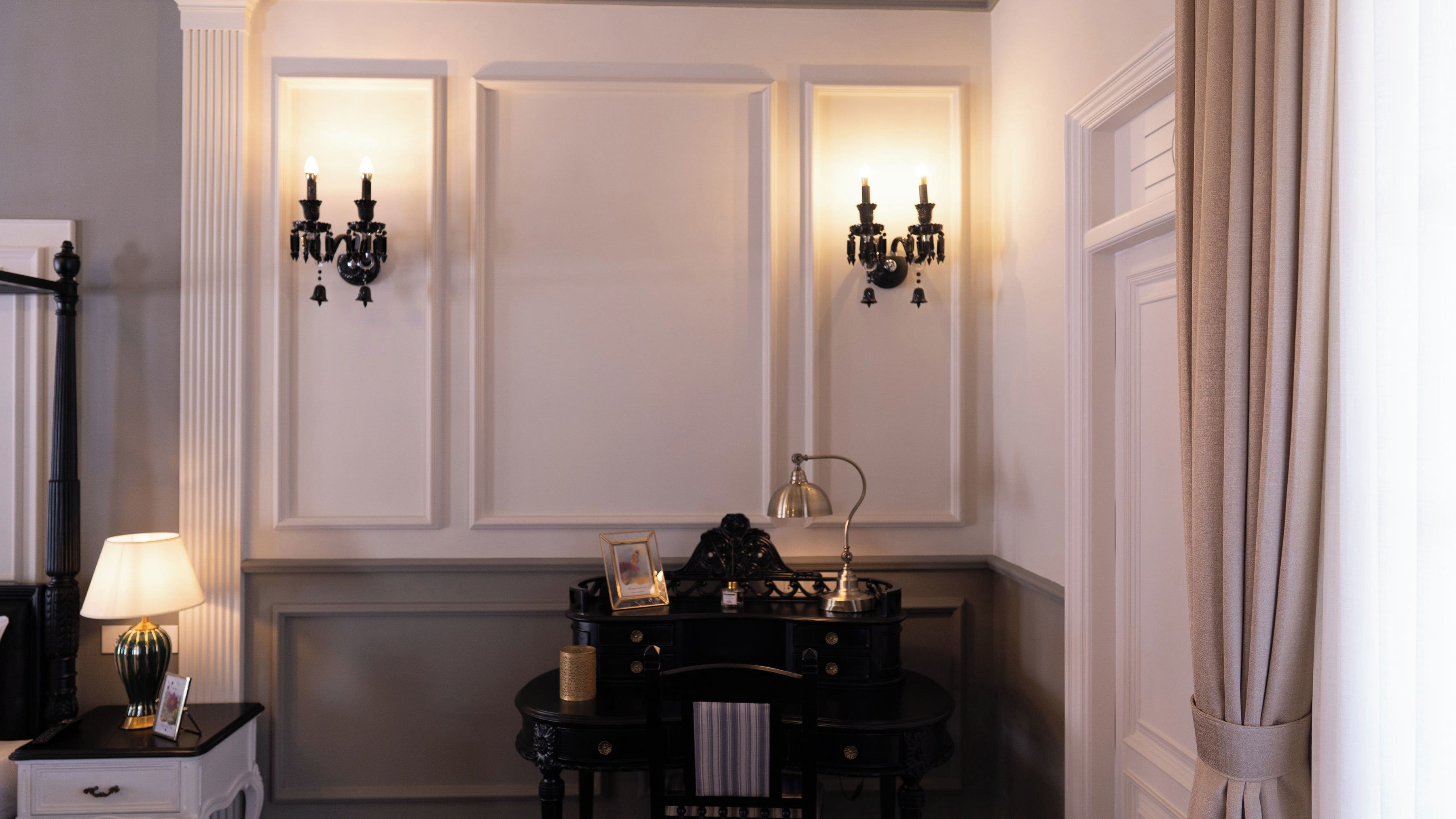 A room with a black console table, a lamp, a framed picture, and wall sconces.