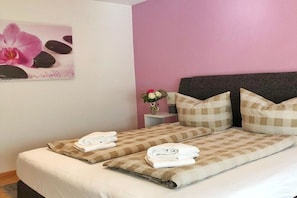A double bed with checkered bedding and folded towels, a nightstand with a vase of flowers, and a wall with a floral artwork. - Holiday home with 4 bedrooms (Garmisch-Partenkirchen)