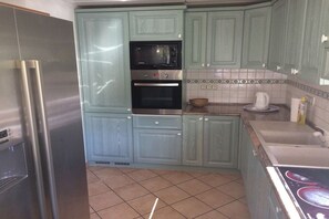 A kitchen with teal cabinets, a stainless steel refrigerator, a double oven, and a tiled backsplash. - Holiday home with 4 bedrooms (Garmisch-Partenkirchen)
