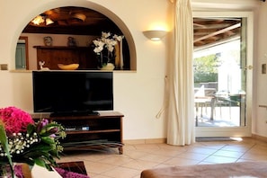A living room with a television, a wooden entertainment unit, a flower arrangement, and a sliding glass door leading to an outdoor area. - Holiday home with 4 bedrooms (Garmisch-Partenkirchen)