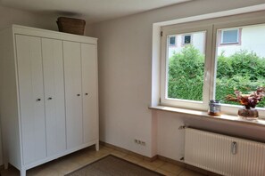 Een kamer met een witte inbouwkast, een raam met uitzicht op groen en een radiator eronder.