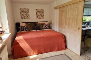 Een slaapkamer met een bed, kussens, een houten deur en een raam met uitzicht.