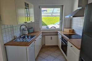 A compact kitchen with a window, a sink, a stove, and a dishwasher. - Holiday apartment with 2 bedrooms (Garmisch-Partenkirchen)
