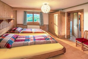 A room with two beds, a wooden wardrobe, a chair, and a window with curtains. - Holiday apartment with 1 bedroom (Wertach)