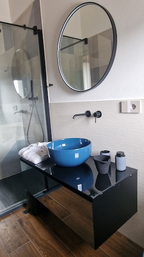 A modern bathroom with a glass shower enclosure, a round mirror, a blue basin, and a black vanity with a towel. - Villa Vinomare in Lunigiana. Infinity hot tub with sea view (Toscana)