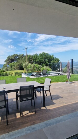 An outdoor seating area with tables and chairs, a pool, and a view of trees and hills. - Villa Vinomare in Lunigiana. Infinity hot tub with sea view (Toscana)