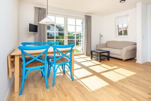 A room with a wooden dining table, blue chairs, a beige sofa, a small black table, and a TV mounted on the wall. - Holiday apartment with 1 bedroom (Lenggries)