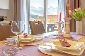 A dining table set with plates, glasses, and cutlery, with a view of mountains through large windows. - Karwendel Lounge at Paschek's Country House (Krün)