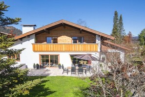 A two-story house with a wooden balcony, a patio with outdoor furniture, and a mountain backdrop. - Karwendel Lounge at Paschek's Country House (Krün)
