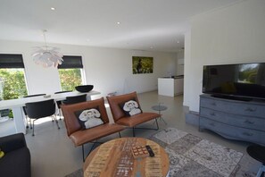 A modern living room with a television, leather sofas, a coffee table, and a dining area with a white table and black chairs. - Holiday home with 2 bedrooms (Oostkapelle)