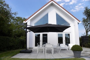 A modern two-story house with a patio area featuring a table and chairs, a large umbrella, and a potted plant. - Holiday home with 2 bedrooms (Oostkapelle)