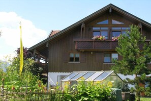 A two-story wooden house with a balcony, a greenhouse, and a garden with various plants. - Mountain view - Apt. Linde (Immenstadt im Allgäu)