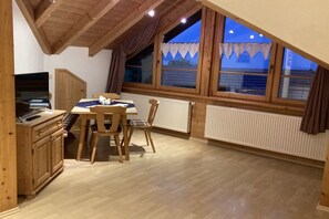 A dining area with a table and chairs, wooden ceiling beams, and a window with curtains. - Mountain view - Apt. Linde (Immenstadt im Allgäu)