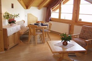 A cozy room with a wooden dining table, chairs, a sofa, and a window with curtains. - Mountain view - Apt. Linde (Immenstadt im Allgäu)