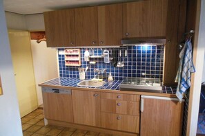 A compact kitchen with wooden cabinets, a tiled backsplash, and a stainless steel sink. - Holiday home in Hollum with swimming pool (Hollum)