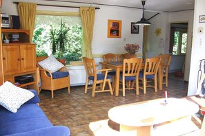 A room with a blue sofa, a dining table with chairs, a wooden cabinet, and a window with curtains. - Holiday home in Hollum with swimming pool (Hollum)