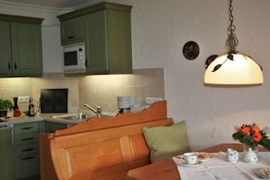 A kitchen with wooden cabinets, a microwave, a sink, and a dining area with a table set for tea. - Holiday apartment with 1 bedroom (Oberstdorf)