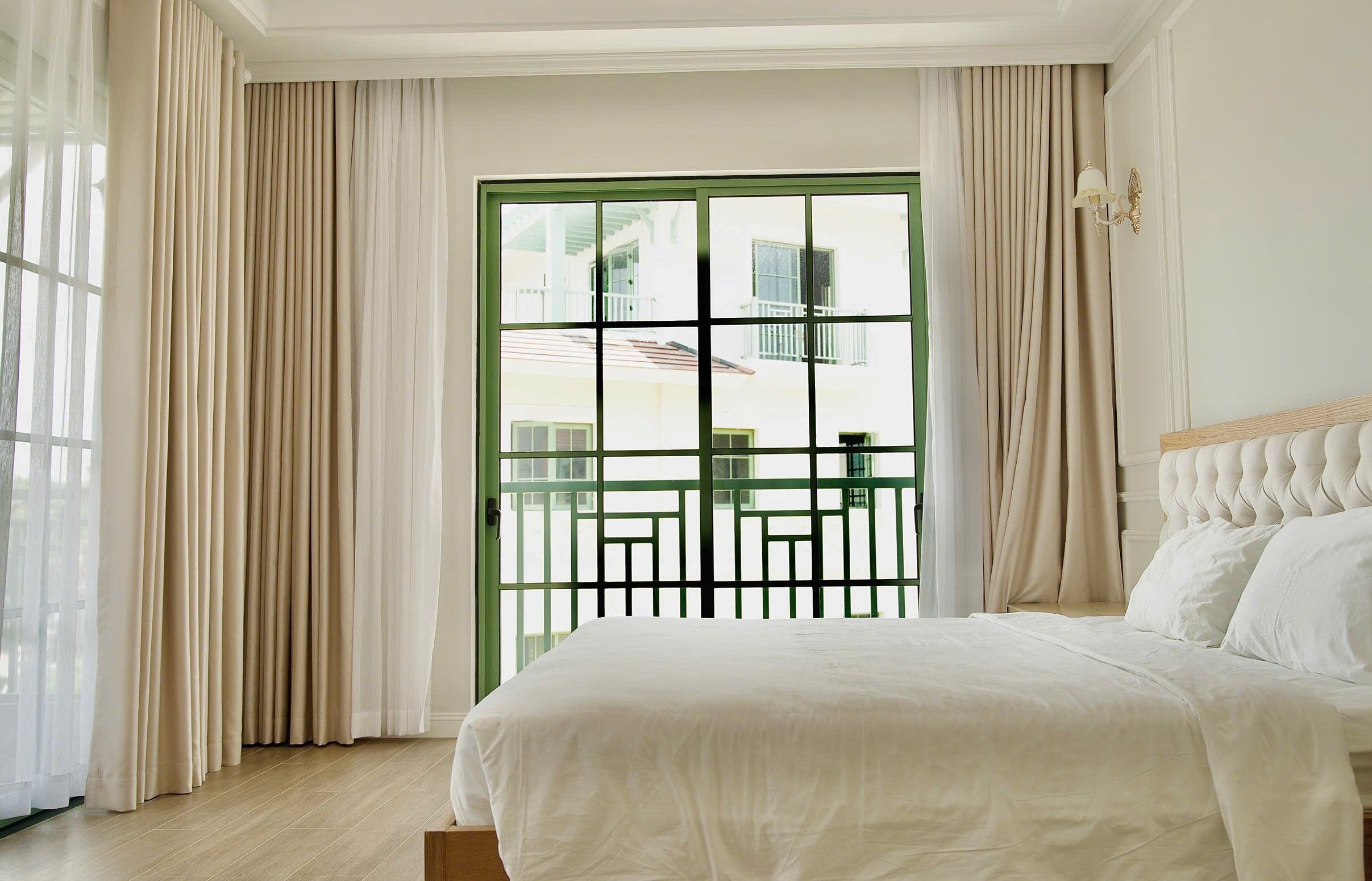 A hotel room with a bed, curtains, a window with a view, and a wall-mounted light fixture.